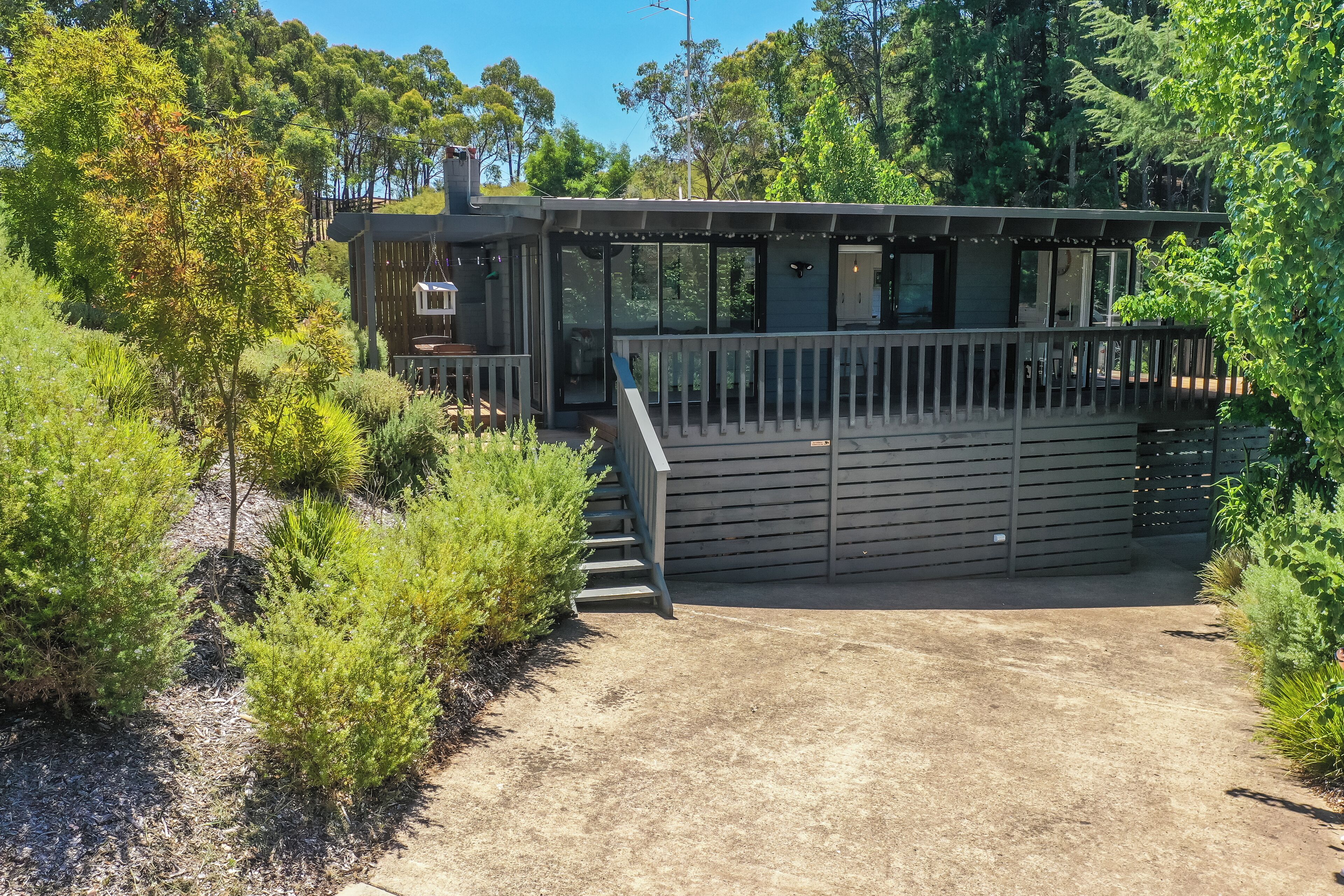 A modern house with a deck, surrounded by lush greenery.