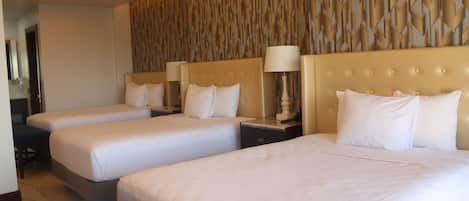 A hotel room with three single beds, a large wall with a geometric pattern, and a modern ceiling design.