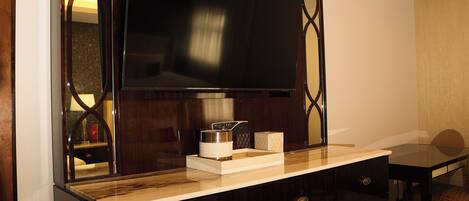 A modern hotel room with a large flat-screen TV mounted on a wooden cabinet, a small table with a tray, and a chair.