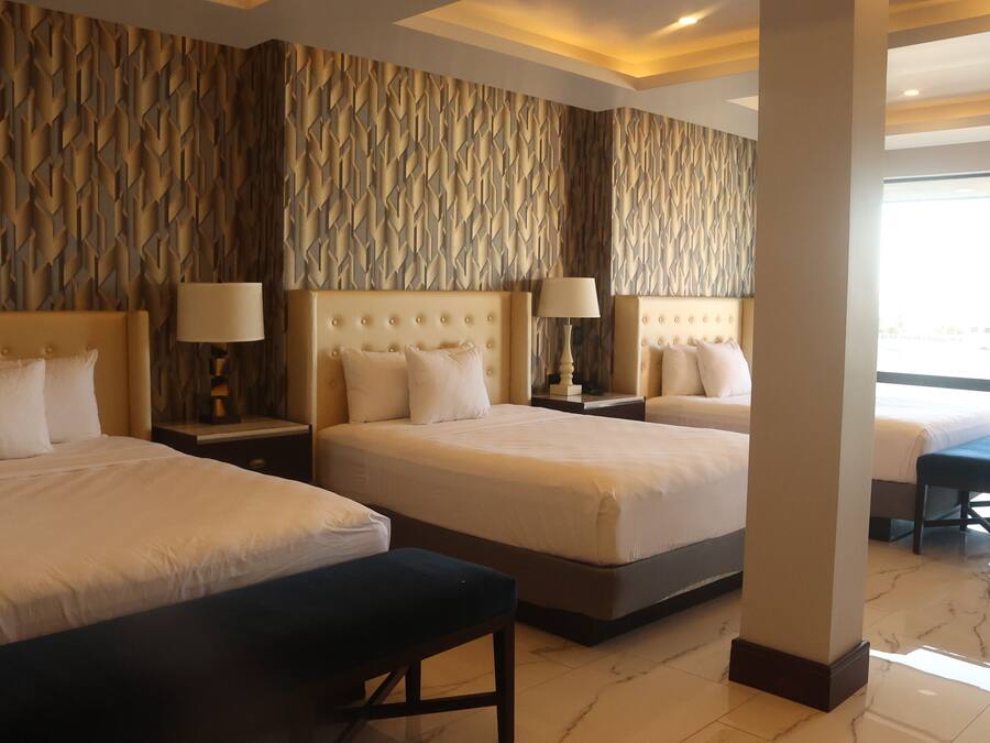 A hotel room with three beds, a bench, and a view of the city.