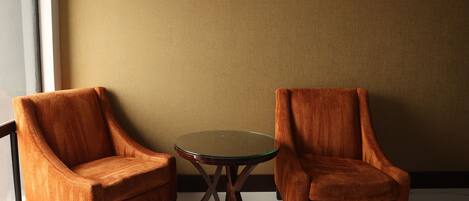 Two armchairs and a glass-top table in a room with a plain wall and a window.