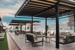 An outdoor lounge area with seating arrangements, a pergola structure, and a view of a high-rise building in the background. - Hotel West Plaza  (Tijuana)
