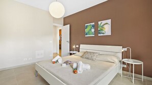 Une chambre à coucher moderne comprenant un lit, des tables de chevet, une petite table d’appoint, une lampe suspendue et deux œuvres d’art murales.