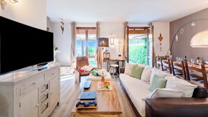 Ein modernes Wohnzimmer mit Flachbildfernseher, Couch, Holztisch und Essbereich mit Stühlen und Tisch.