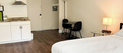 Une chambre d’hôtel avec un grand lit, un bureau avec une chaise, une petite table avec une lampe et un coin cuisine.