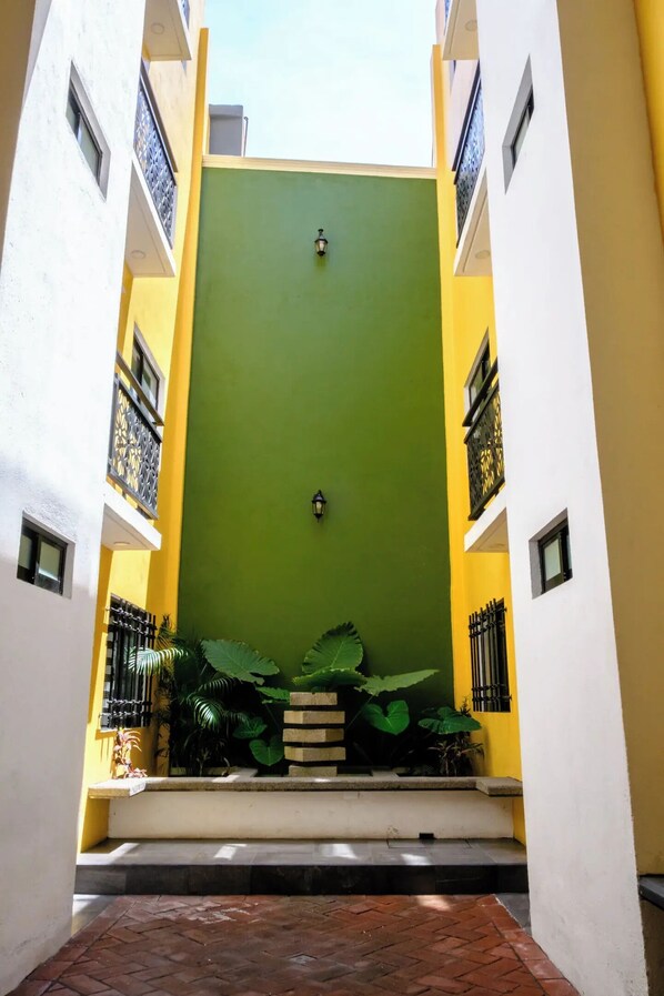 Un patio estrecho con una puerta verde, paredes amarillas y suelo de baldosas.