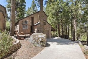 A two-story house with a stone facade, a large rock in the front yard, and a paved driveway.