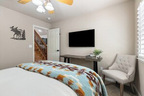 A bedroom with a bed, a chair, a television, and a staircase.