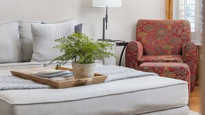 Un salón con un sofá, un sillón estampado, una mesita con una bandeja y una planta en maceta.