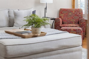 A living room with a sofa, a patterned armchair, a small table with a tray, and a potted plant.