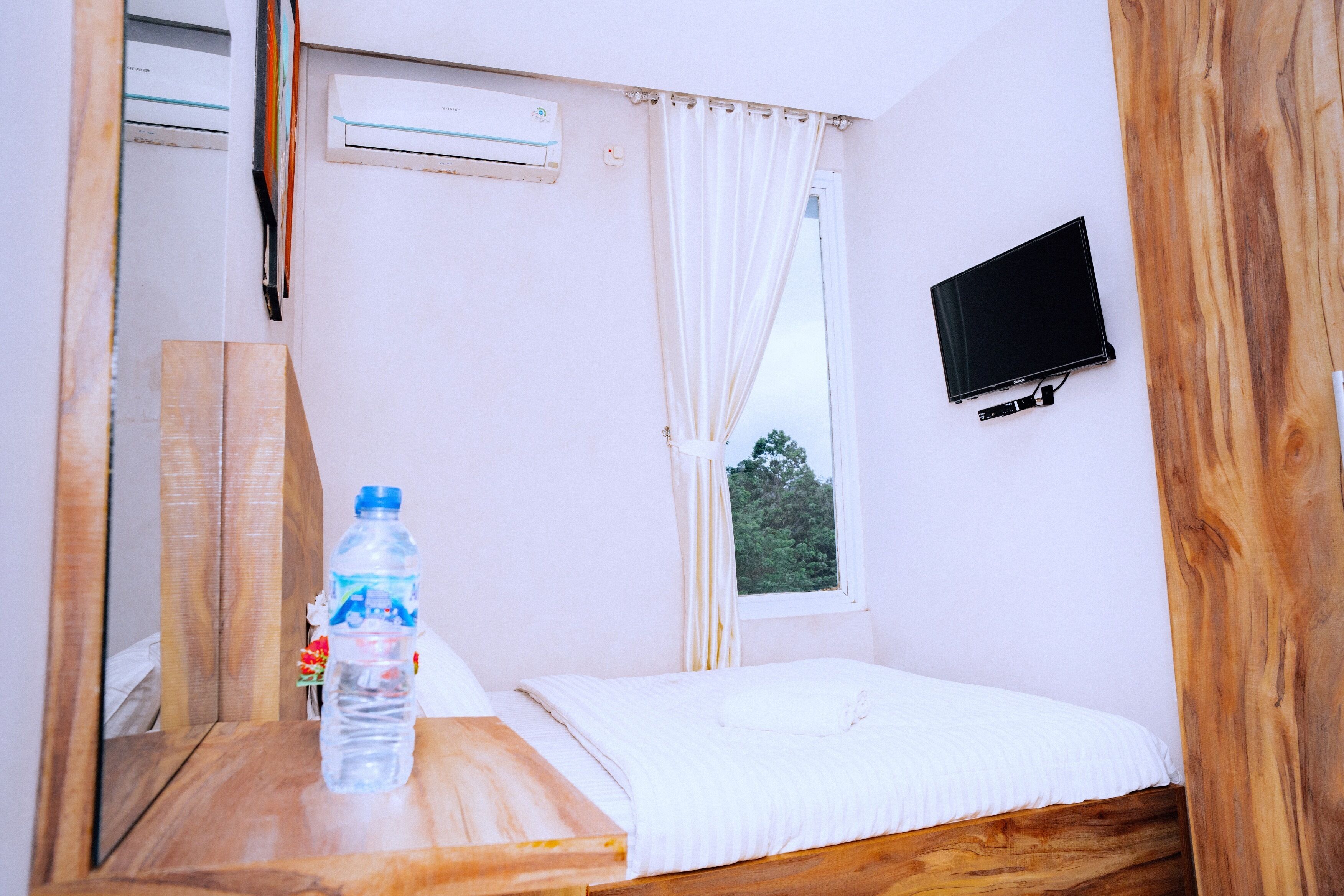 Una stanza piccola e semplice con un letto, una TV fissata al muro, una finestra con tende e un condizionatore d'aria.