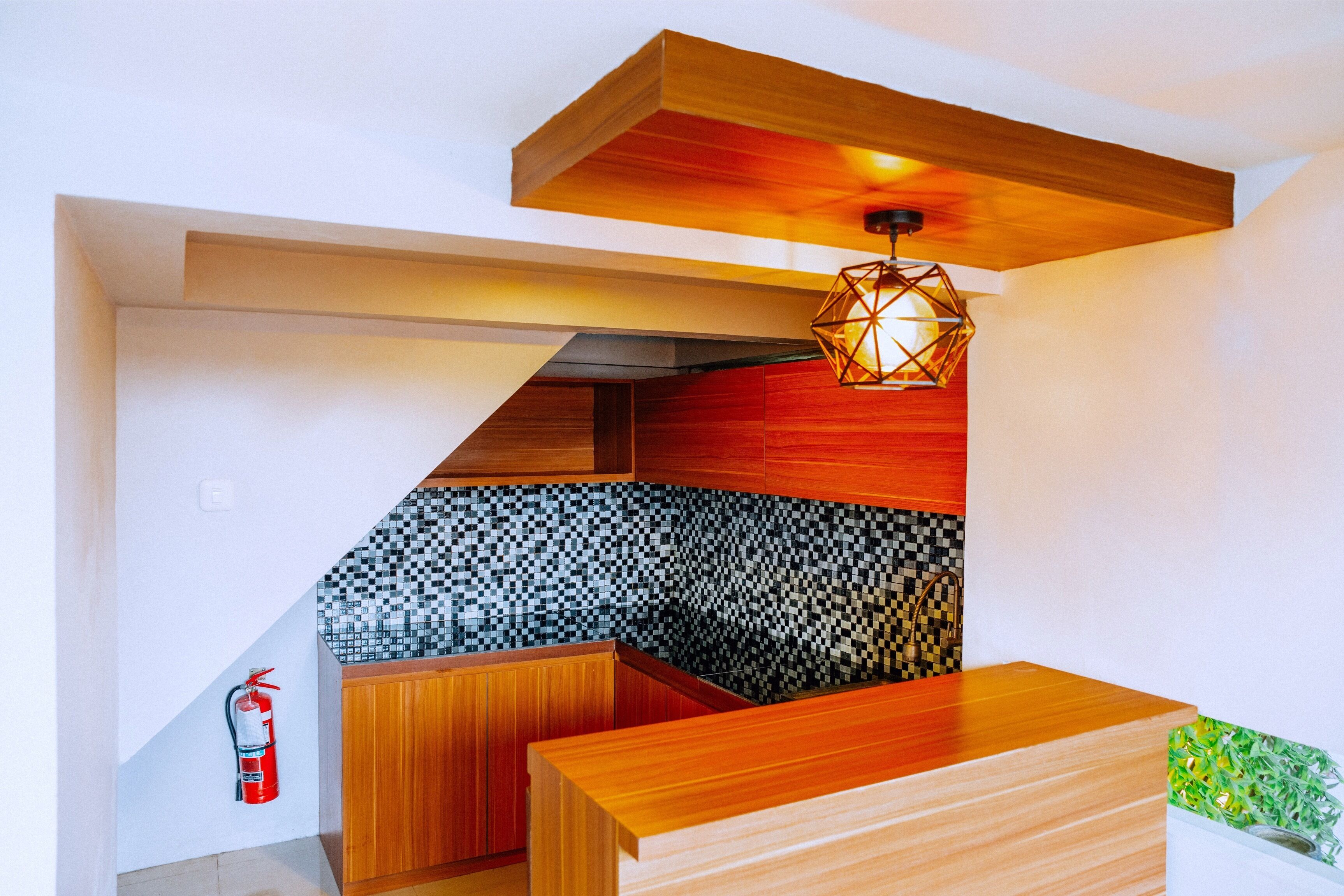 Una cocina moderna con armarios de madera, un protector contra salpicaduras a cuadros y una lámpara colgante de diseño geométrico.