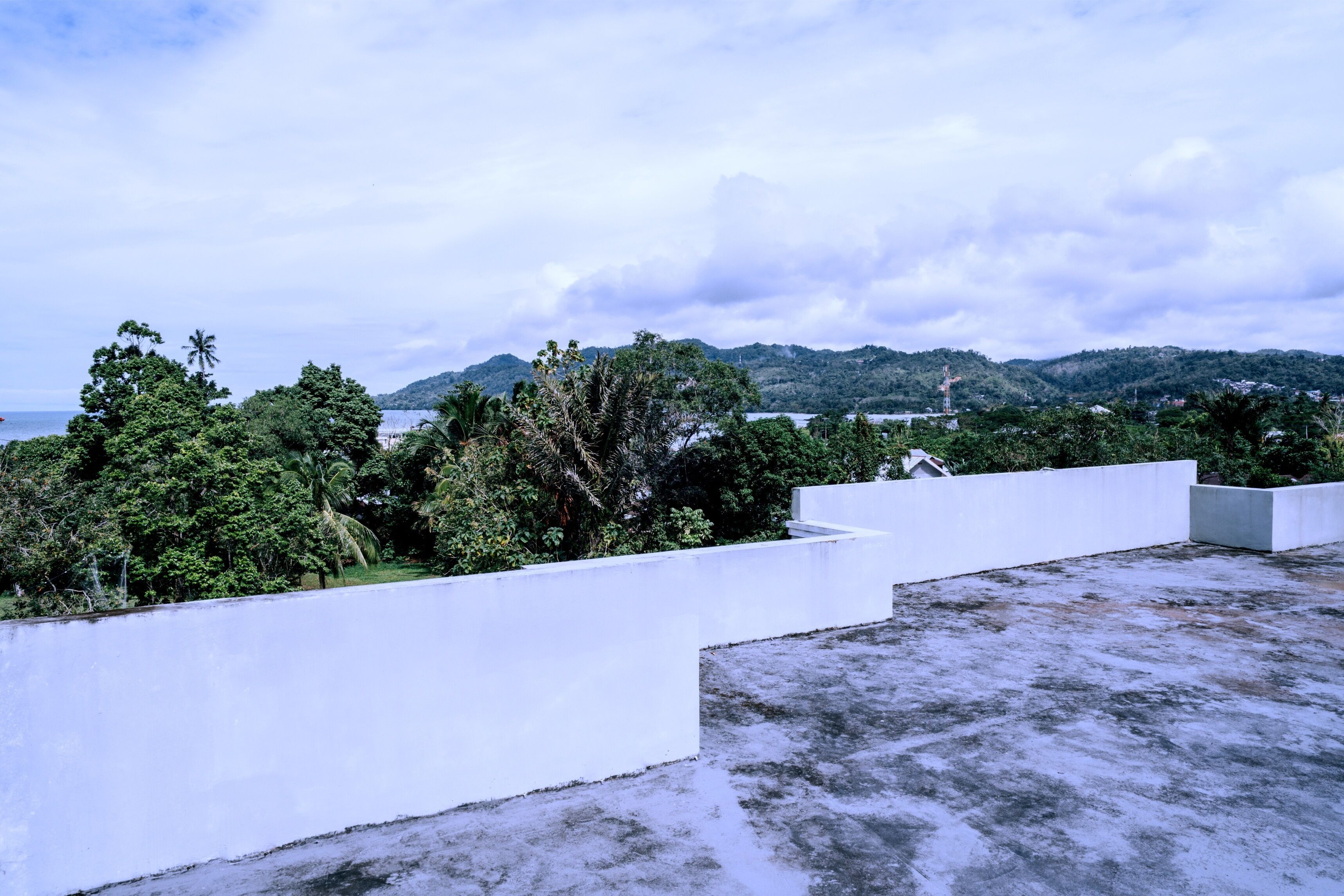 A rooftop terrace with a white wall, greenery, and a view of hills and water.