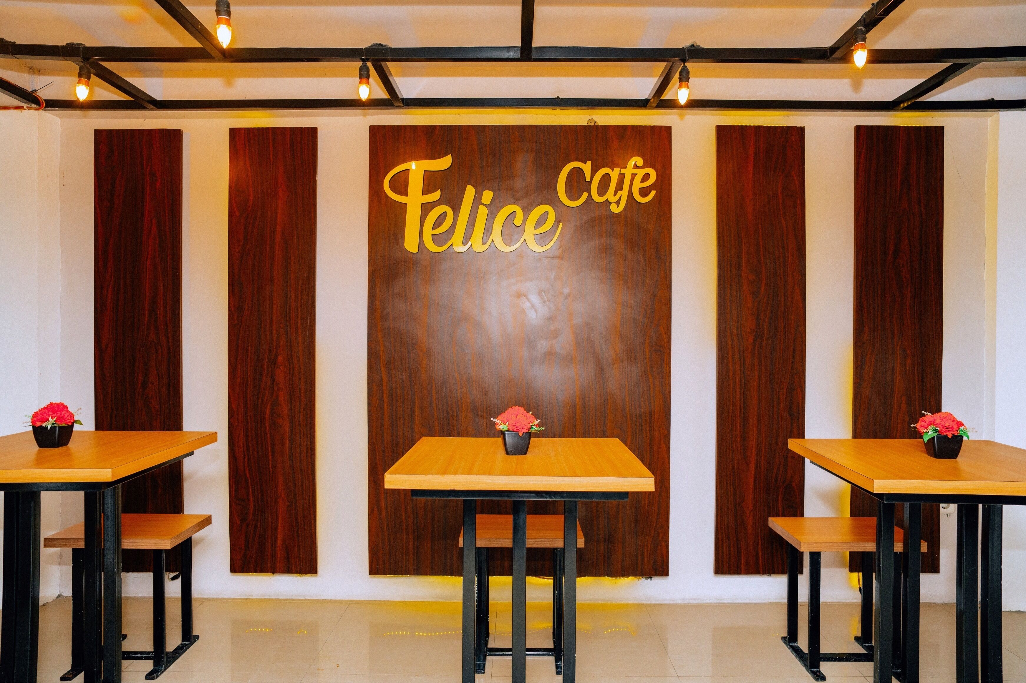 A cafe interior with wooden panel walls, a central table with a flower vase, and two smaller tables with chairs.