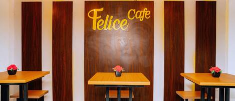 A cafe interior with wooden panel walls, a central table with a flower vase, and two smaller tables with chairs.