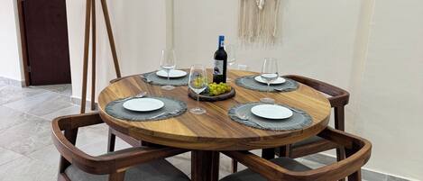 Een ronde houten eettafel met vier stoelen, een fles wijn en een decoratieve macramé wandversiering.