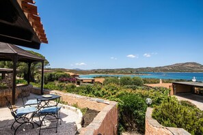 Eine Terrasse mit Gartenmöbeln, einer Pergola und Blick auf das Meer und die Hügel.