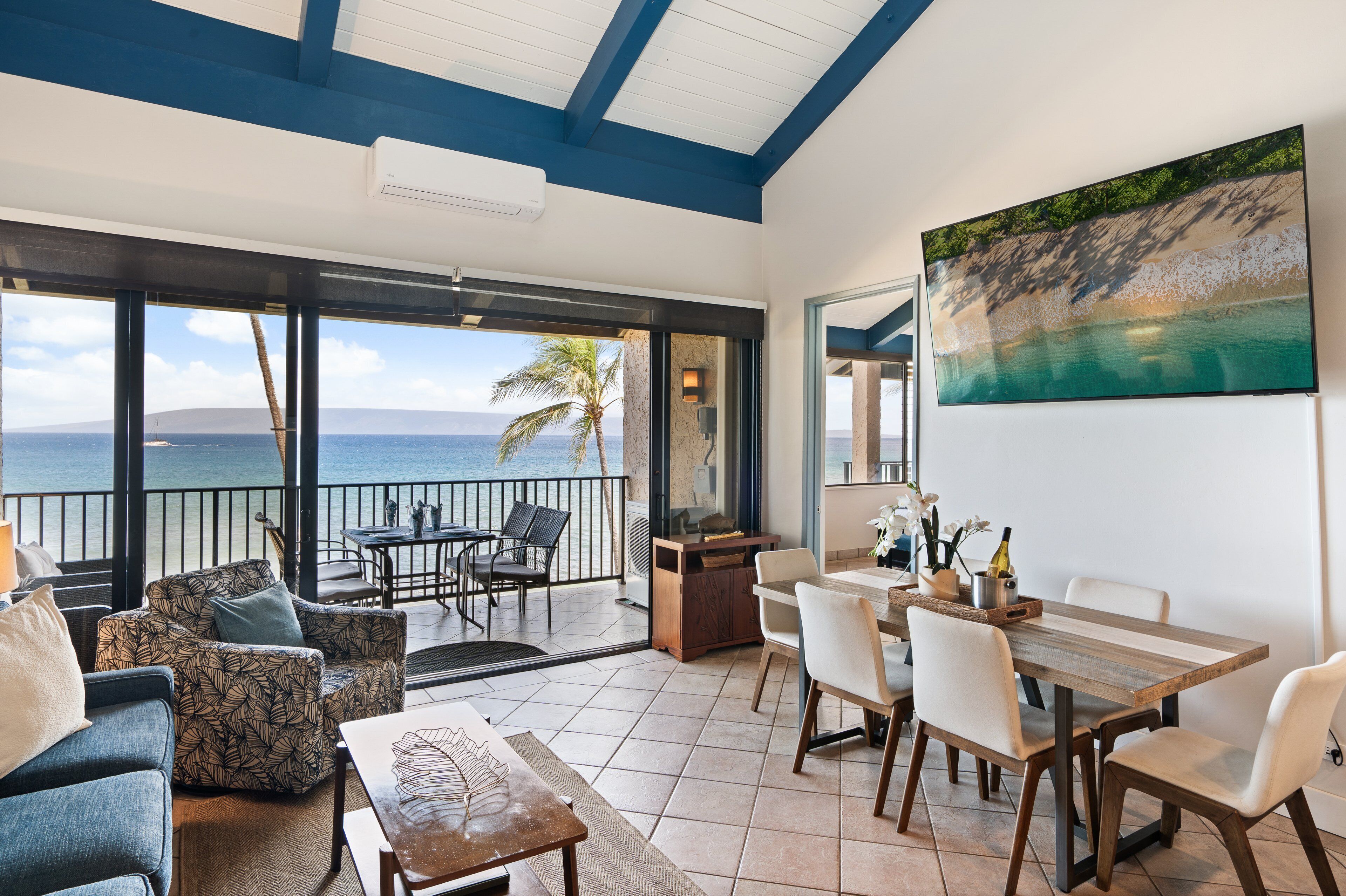 A spacious balcony with a view of the ocean, a dining area with a table and chairs, and a large painting on the wall.