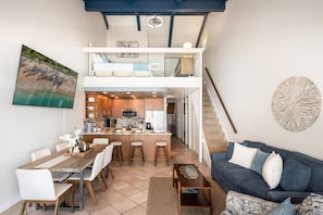 A modern interior with a dining area, kitchen, and living space, featuring a staircase and a view of the outdoors.