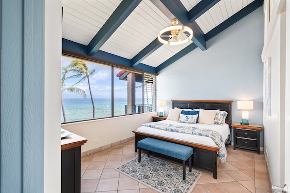 A bedroom with a large window, a bed, a bench, and a ceiling fan.