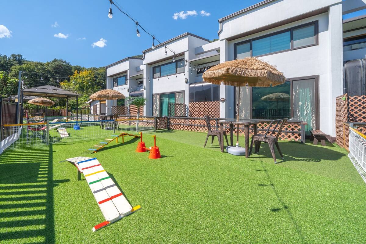 Un espace de jeux extérieur moderne, doté d’une pelouse artificielle, d’aires de jeux et de sièges extérieurs.