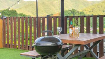 A barbecue grill on a wooden table with a bottle and a glass on it.