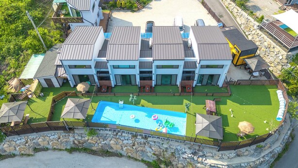 A modern multi-story building with a swimming pool, outdoor seating, and a stone retaining wall. - Gapyeong Beilli pet Pool Villa Pension (Gapyeong)