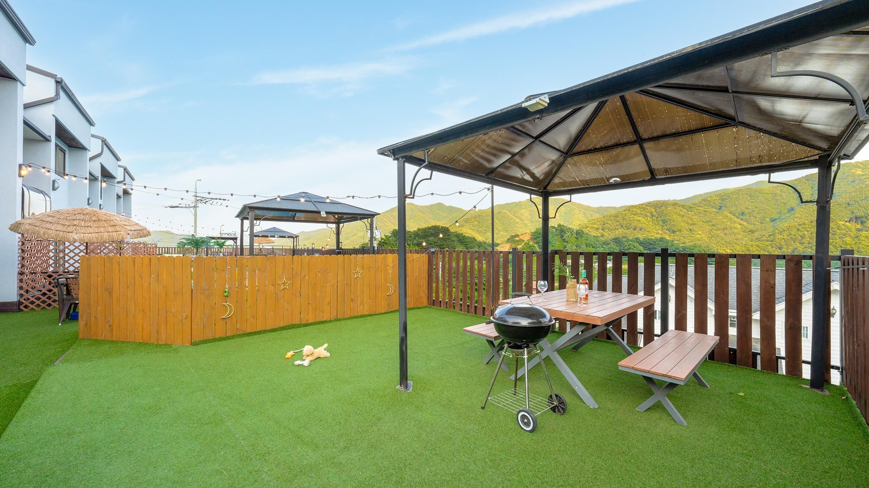 A backyard with artificial grass, a barbecue grill, wooden picnic table, and a wooden fence.