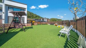 Un jardin avec une pelouse artificielle, une balançoire et une clôture en bois.