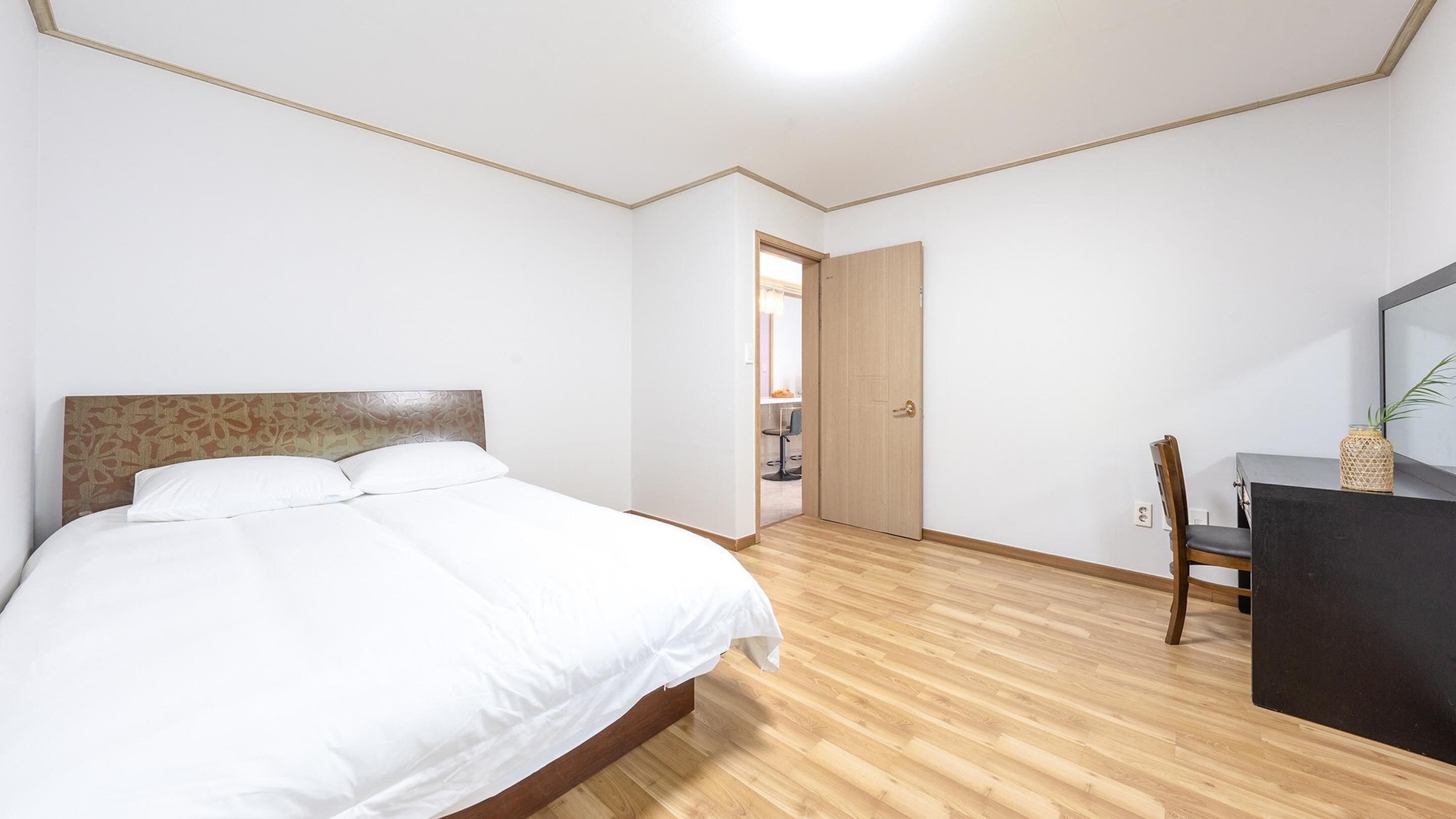 A bedroom with a bed, a desk, and a chair. There is a door leading to another room.