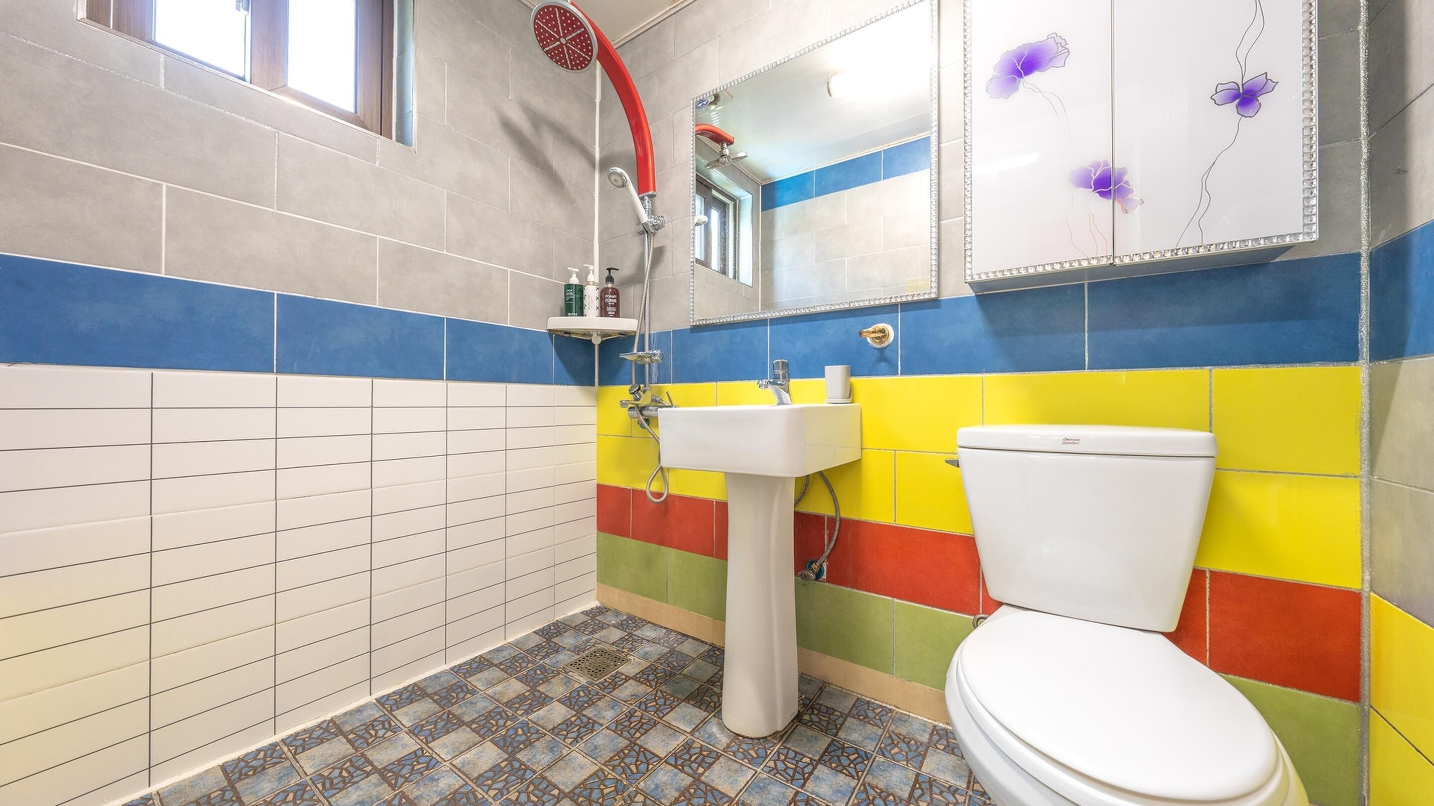 A bathroom with a white toilet, a sink, and a shower. The walls are tiled in blue, yellow, and red.