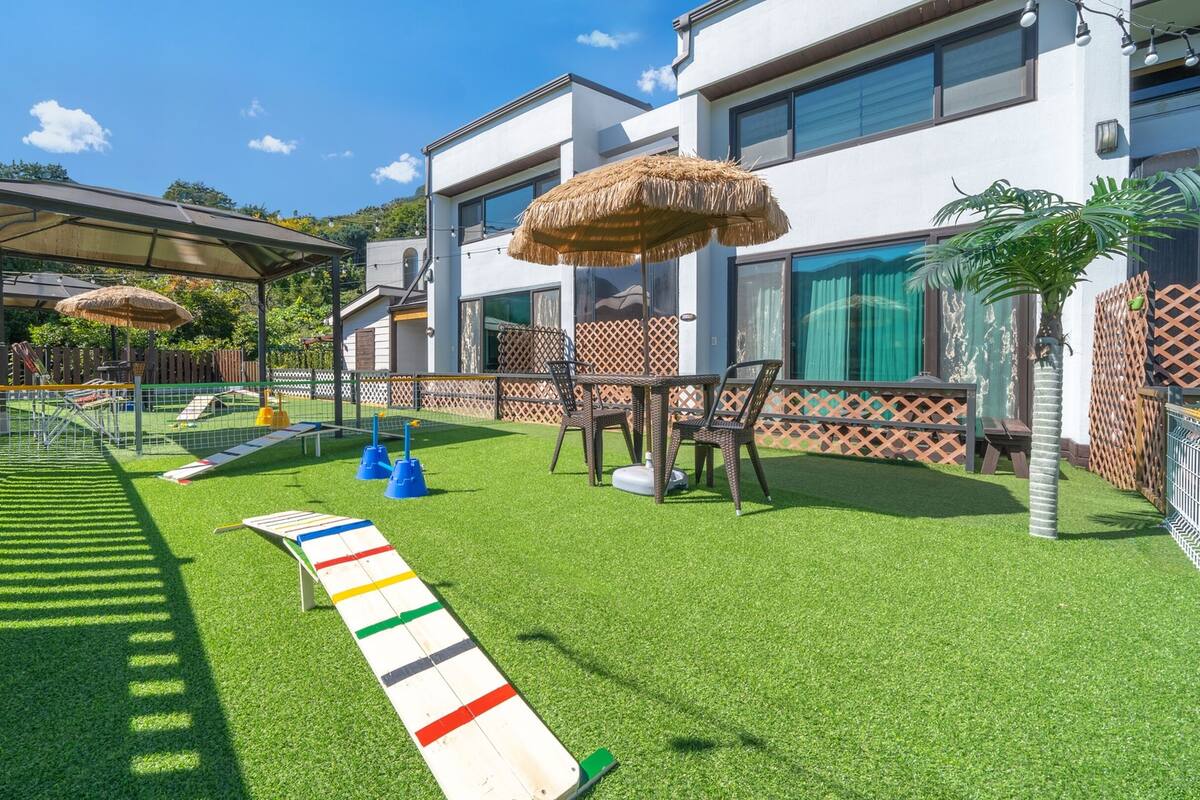 Un espace de jeux pour enfants avec une pelouse artificielle, une structure d’escalade et une table de pique-nique.