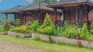 A wooden cabin with a porch, surrounded by lush vegetation and a clear sky.