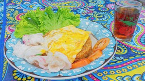 A plate of food with an omelette, vegetables, and a glass of tea on a colorful tablecloth.