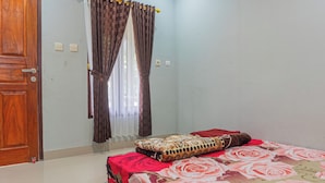 A bedroom with a bed, curtains, a wooden door, and a light switch.
