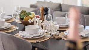 Een eetgedeelte met een tafel voor twee, compleet met borden, kommen, glazen en een middelpunt met fruit en een zoutvaatje.