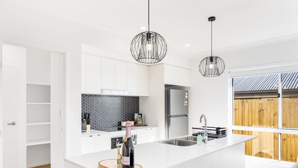 Een moderne keuken met witte kasten, een zwarte spatwand en een centraal kookeiland met een fles champagne.