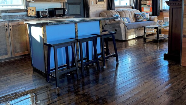 Amplia sala de estar con piso de madera, un sofá, una mesa de centro y una zona de cocina con barra y taburetes.
