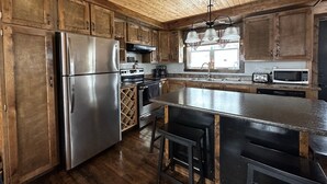 Cocina rústica con armarios de madera, electrodomésticos de acero inoxidable y una isla central con taburetes de bar.