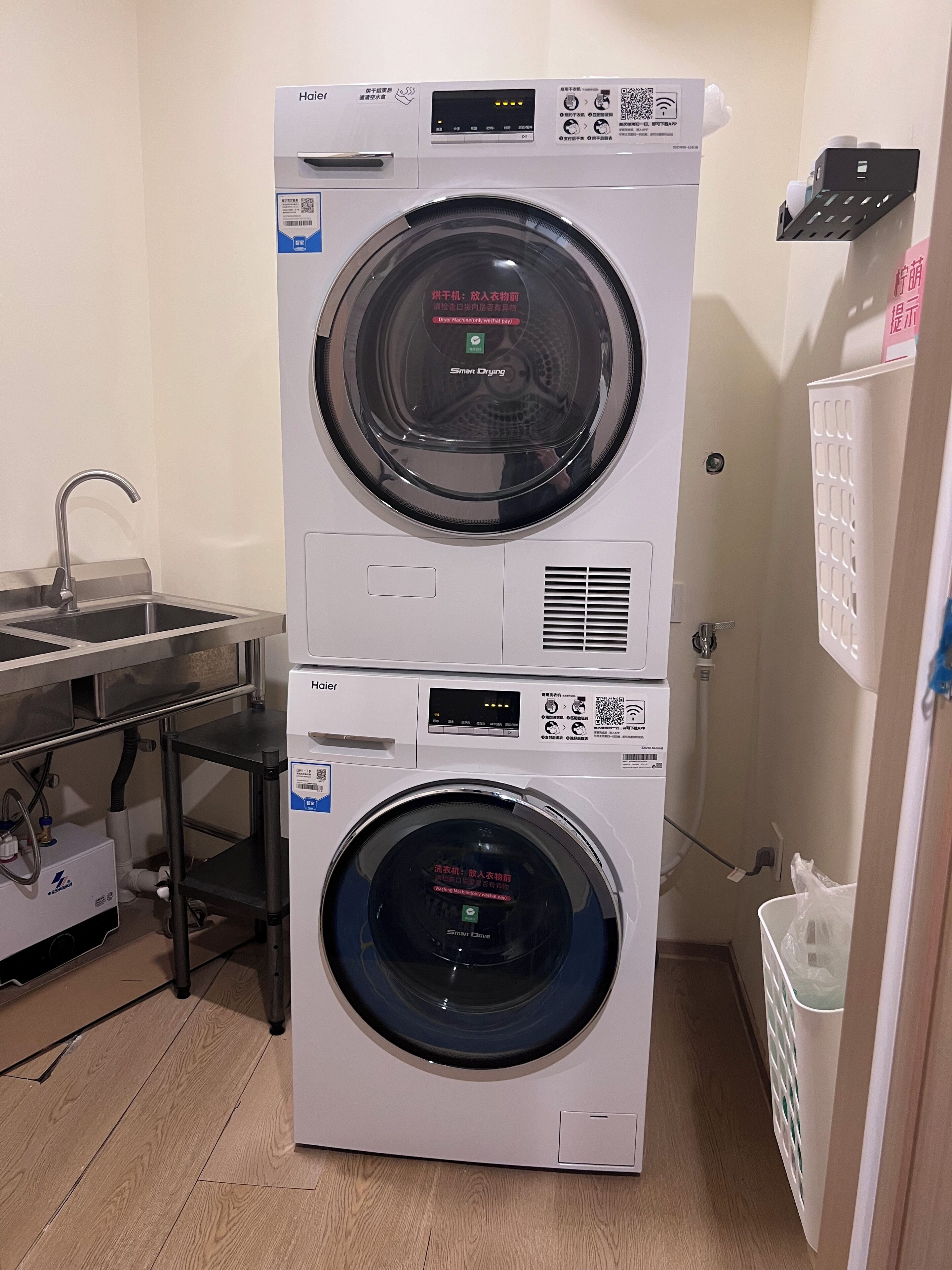 A stacked washer and dryer unit in a laundry room with a sink and a metal shelf.