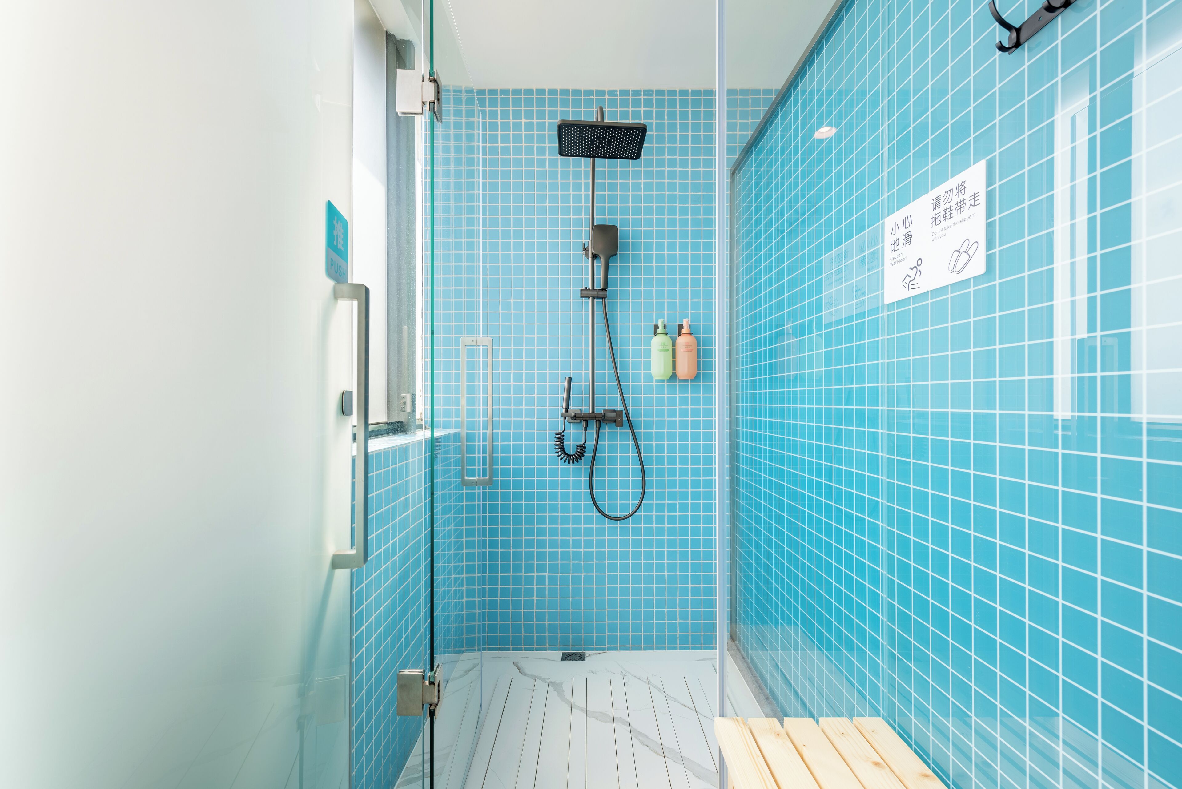 Een badkamer met blauwe betegelde wanden, een douche met handdouche en een houten bankje.