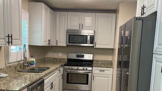 A kitchen with white cabinets, a stainless steel microwave, oven, and refrigerator, and a granite countertop. - Home with a large yard-Minutes from Downtown!!! (Beaufort)
