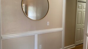 A hallway with a round mirror on the wall, wooden flooring, and a door at the end. - Home with a large yard-Minutes from Downtown!!! (Beaufort)