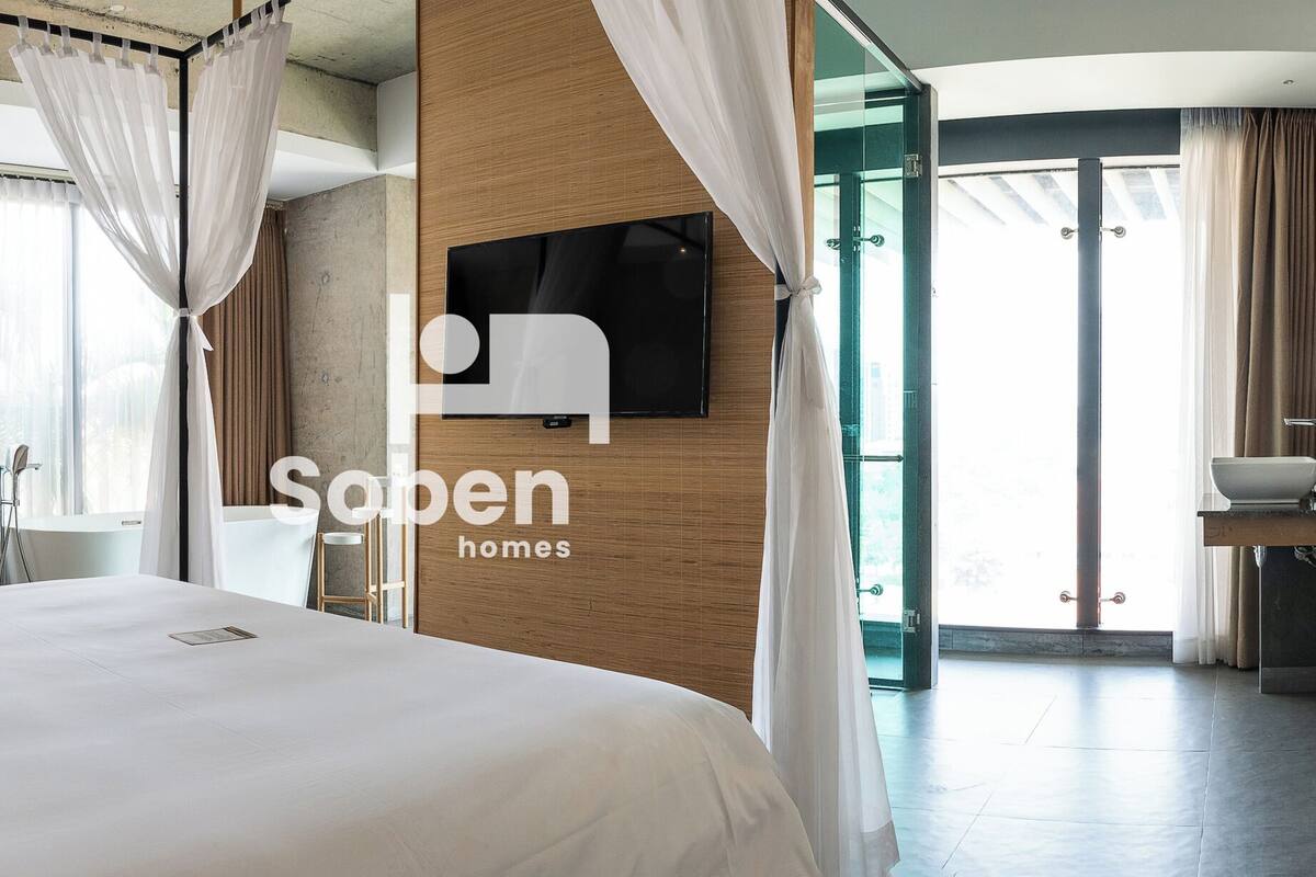 A hotel room with a large bed, a TV mounted on the wall, a bathroom with a sink, and a shower.