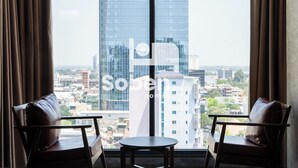A room with two leather chairs and a small table, a large window with a city view, and a visible logo. - Royal Palace Suites Phnom Penh by Soben (Phnom Penh)