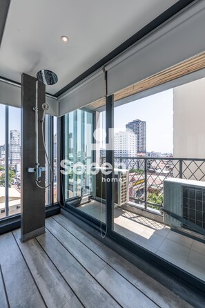 Un balcón moderno con puerta de cristal, una ducha y vistas de la ciudad.