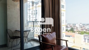 A balcony with a view of the city, a brown leather chair, a small table, and a black chair. - Royal Palace Suites Phnom Penh by Soben (Phnom Penh)