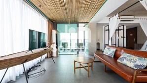 A modern hotel room with a wooden ceiling, a large window, a sofa, and a TV. - Royal Palace Suites Phnom Penh by Soben (Phnom Penh)