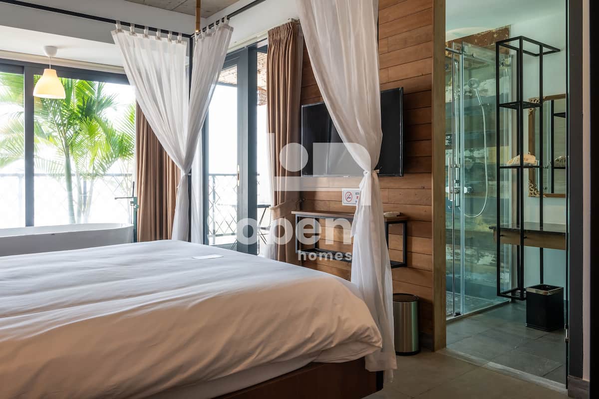 A modern hotel room with a large bed, a TV mounted on the wall, and a glass shower enclosure.
