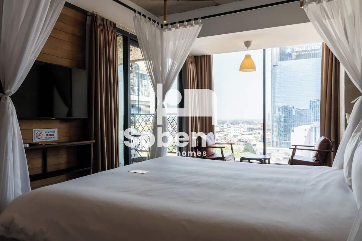 A hotel room with a large bed, a TV, a balcony with a view of the city, and a 'No Smoking' sign.